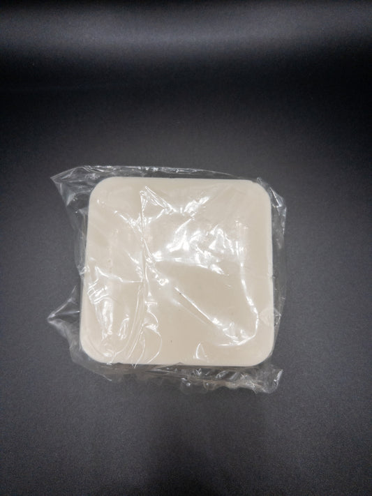 A picture of a square bar of soap that is beige on top and infused with turmeric and honey. It is sitting on a black background.