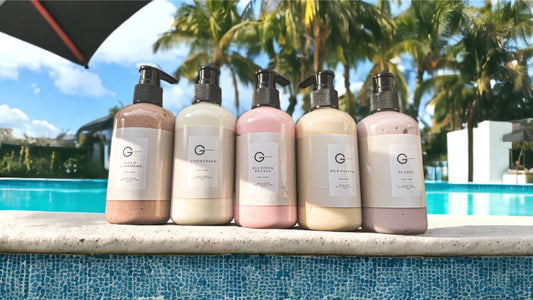 Picture of 5 bottles of body cream on the side of a pool with palm trees in the background.